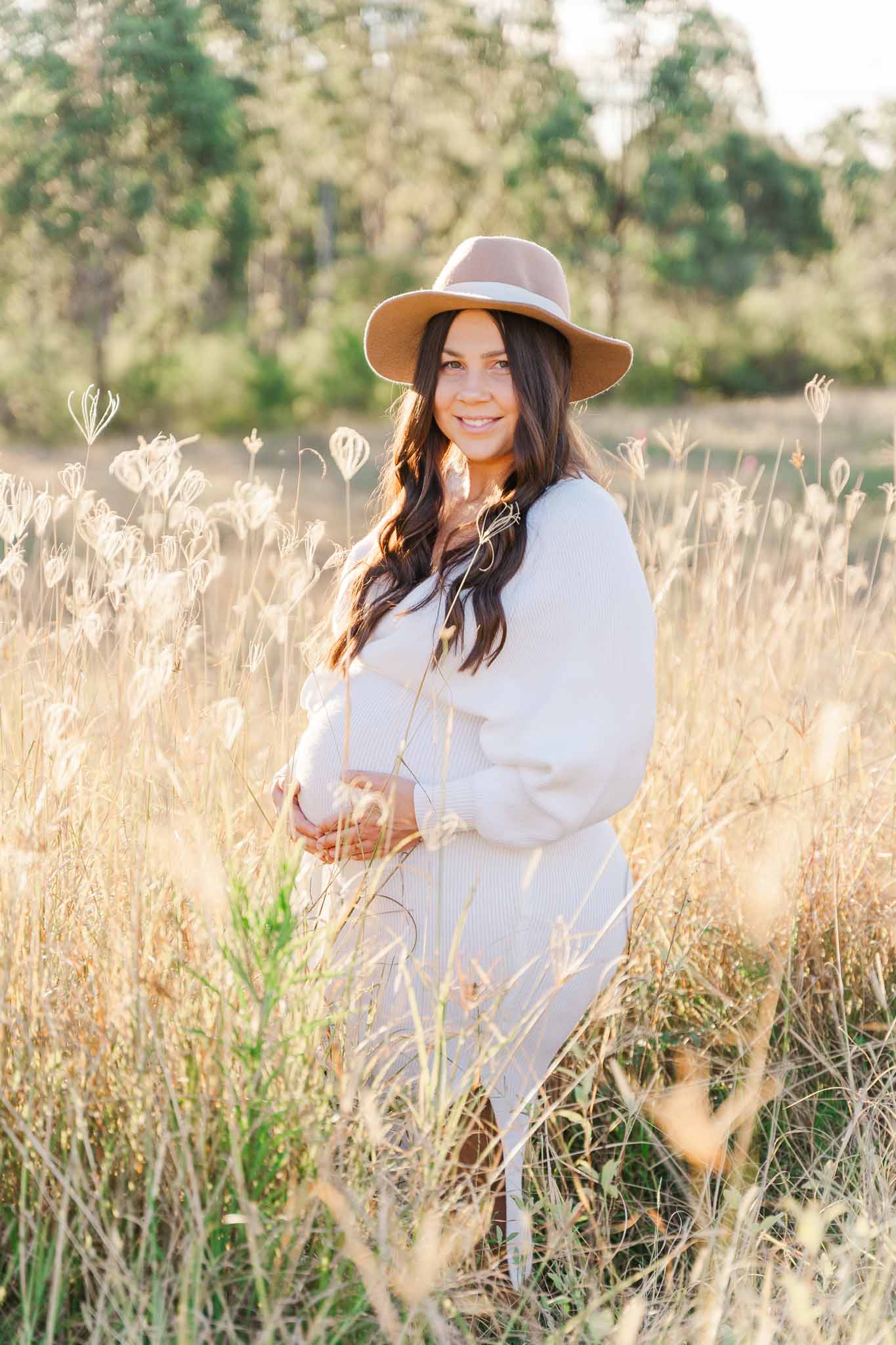 Pregnant woman standing in a field of wait high golden grass during her maternity photo shoot